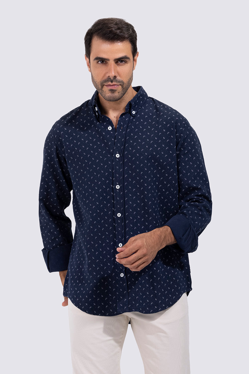 Man wearing a navy blue patterned shirt and white pants on a light gray background